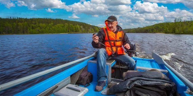man in life jacket using electronic compass on his boat on the water