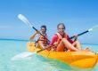 Father and daughter in life jackets on a kayak on the water holding paddles